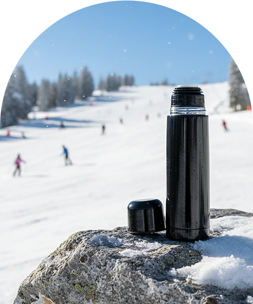 En svart termos p&aring; en sn&ouml;t&auml;ckt sten, med en skidbacke i bakgrunden.
